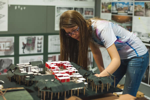 an architecture student works on a model with sticks and paper 