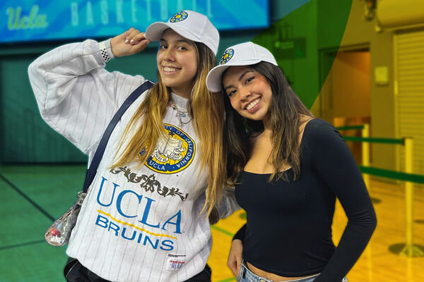 two women smiling wearing college hats and a sweatshirt